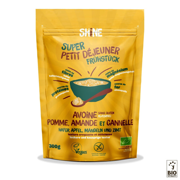 Lemballage jaune des céréales Avoine Pomme, Amande et Cannelle Bio de SHINE met en valeur la pomme, lamande et la cannelle. Elles sont sans gluten, végétaliennes, biologiques et bilingues en français et en allemand. Profitez de la richesse du beurre damande à chaque bouchée !.